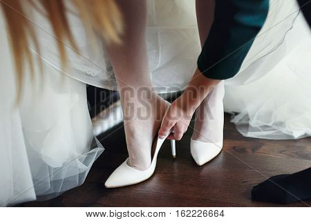 Bridemaid helps bride to put shoes on