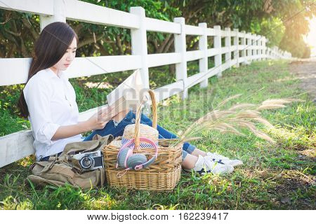 Pretty relaxed young asian woman reading a book at the lawn garen with sun shining vintage tone.