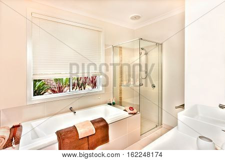 Luxury washroom prepared with towels and soap in the white color bath tub bathing area covers with the glass room next to the water tub. A washstand from the right side