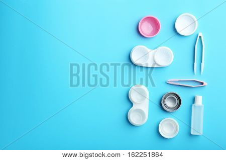 Containers for contact lenses, tweezers and bottle of solution on blue background