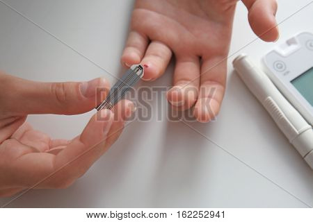 Woman checking blood sugar level by glucometer and test stripe at home