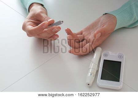 Woman checking blood sugar level by glucometer and test stripe at home