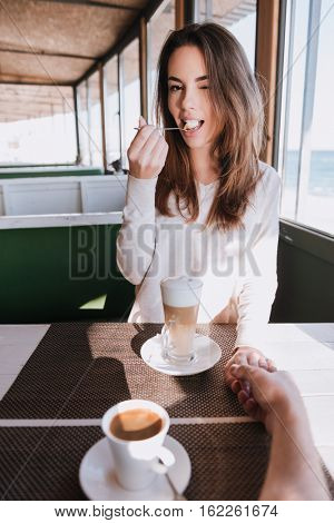 Vertical image of pretty woman on date with coffee in cafe near the sea. First-person view