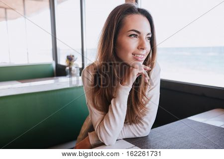 Woman sitting by the table on date in cafe near the sea and looking away