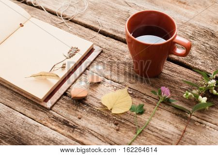 Vintage album with herbarium plants and hourglass with cup of tea on old wooden background. Transience of time, memory, nostalgia, art, hobby concept
