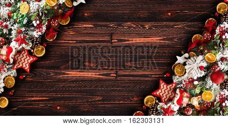Merry Christmas Frame with green pine, colorful baubles, knots with berries,stars, orangesand other seasonal stuff over an old wooden aged background