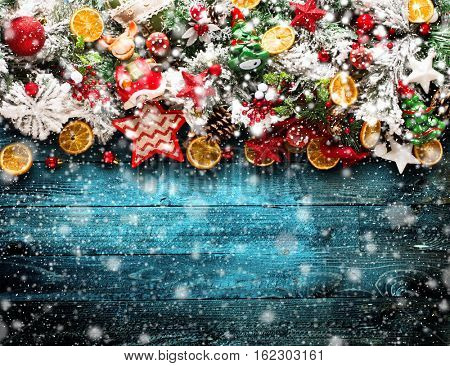 Merry Christmas Frame with Snow and wood green pine, colorful baubles, knots with berries,stars, orangesand other seasonal stuff over an old wooden aged background