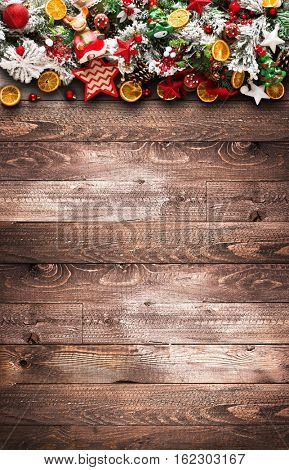 Merry Christmas Frame with green pine, colorful baubles, knots with berries,stars, orangesand other seasonal stuff over an old wooden aged background