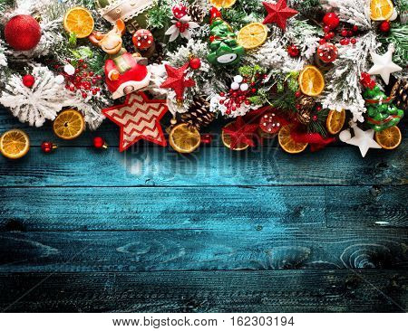 Merry Christmas Frame with green pine, colorful baubles, knots with berries,stars, orangesand other seasonal stuff over an old wooden aged background