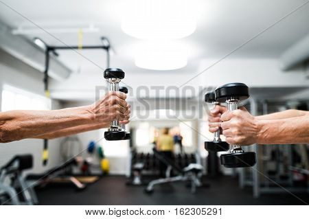 Close up of hands of senior couple in gym working out with weights