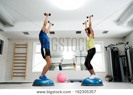 Beautiful fit senior couple in gym working out with weights