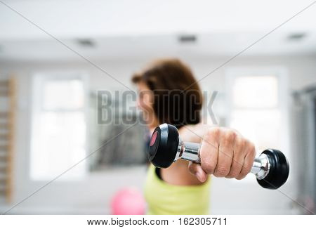 Senior woman in sports clothing in gym working out with weights. Close up of hands.