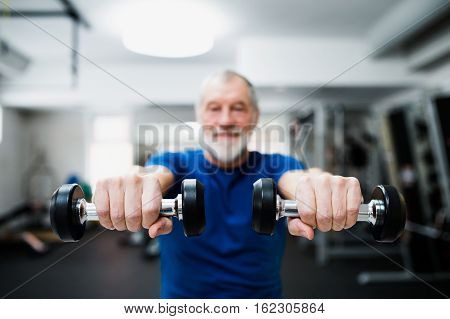 Senior man in sports clothing in gym working out with weights. Close up of hands.
