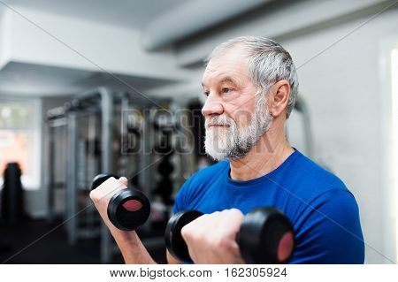 Senior man in sports clothing in gym working out with weights.