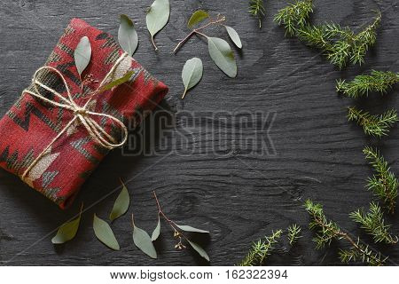 Red fabric present on a black wooden table with eucalyptus and fir tree decoration.