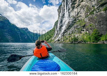 Woman kayaker in bright orange life vest on her trip in Geiranger fjord waters. Geiragerfjord, Norway.