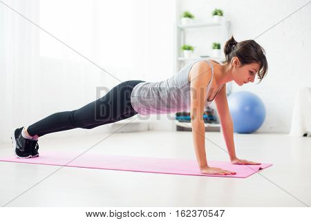fit woman doing push-ups on the floor in her living room on an exercise mat at home