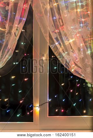 Christmas lights in the window on the background of transparent tulle.
