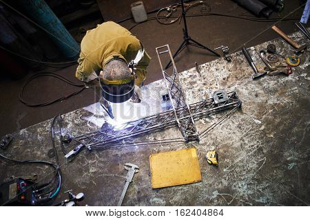 Welder welding metal layout of a construction crane on the iron table