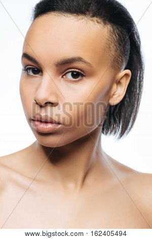Without emotions. Concentrated unemotional young Negroid woman looking at the audience while standing against white background and posing