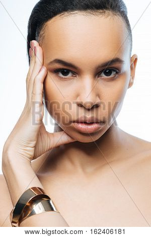 Graceful model. Elegant pathetic young Negroid woman touching her face while standing isolated in white background and expressing grace