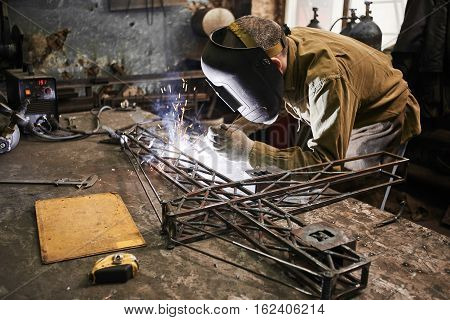 Welder welding metal layout of a construction crane on the iron table