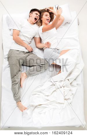 The young lovely couple lying in a bed with phone, love lconcept, top view
