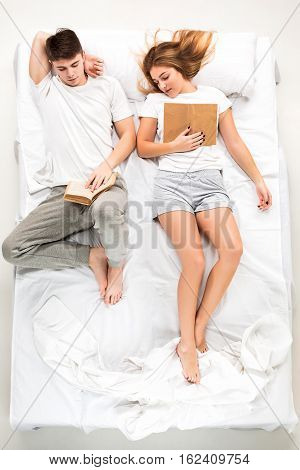 The young lovely couple lying in a white bed with books, love lconcept, top view