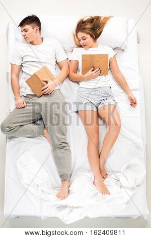 The young lovely couple lying in a white bed with books, love lconcept, top view