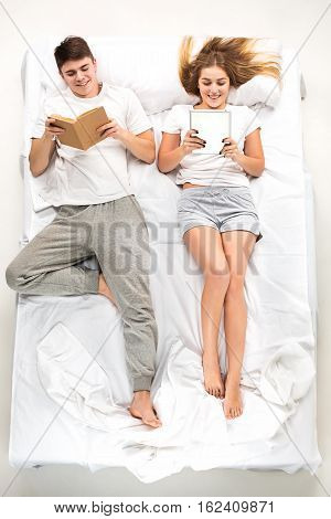 The young lovely couple lying in a white bed with books, love lconcept, top view