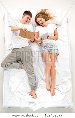 The young lovely couple lying in a white bed with books, love lconcept, top view