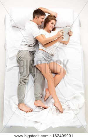 The young lovely couple lying in a white bed with laptop, love lconcept, top view