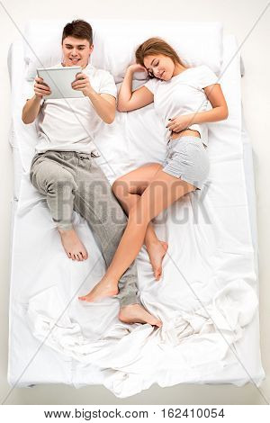 The young lovely couple lying in a white bed with laptop, love lconcept, top view