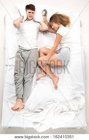 The young lovely couple lying in a white bed with alarm clock, love lconcept, top view