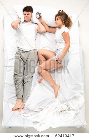 The young lovely couple lying in a white bed with alarm clock, love lconcept, top view