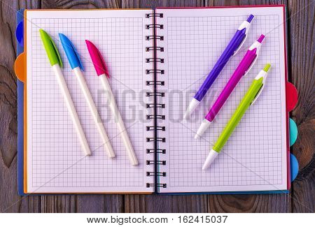 Diary (notebook) and colored pens on wooden background.