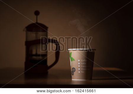 Papaer coffee mug with hot liquid in it and steam over it and cafetiere in background