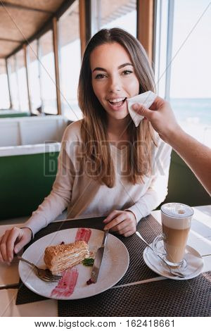 Verical image of pretty woman sitting by the table on date in cafe near the sea and her man wipes her cheek. First-person view