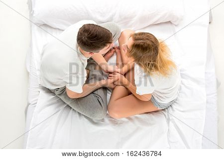 The young lovely couple sitting in a white bed, love lconcept, top view