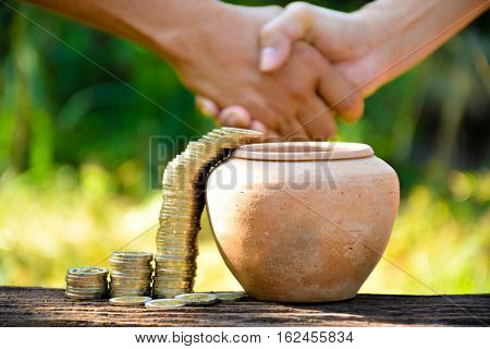 The old earth ware and coin stack almost drop in earth ware and hand of people shake hand