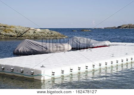 White plastic pontoon for boats and two covered boats in sunny day