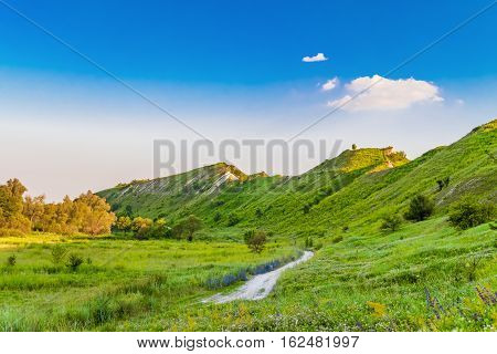 Path at the foot of ridge chalk hills. Green hills under blue sky. The archaeological monument - Krapivinskaya settlement Belgorod region Russia.