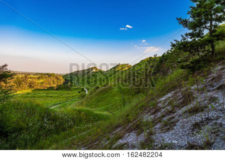 Path at the foot of ridge chalk hills. Green hills under blue sky. The archaeological monument - Krapivinskaya settlement Belgorod region Russia.