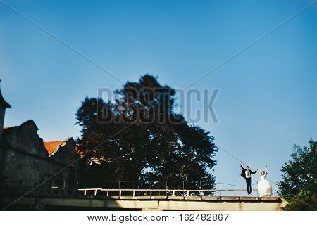 Bride And Goom Jump Behind An Old Castle On Bright Summer Day