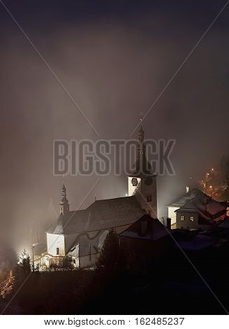 Winter in Slovakia. Old mining village. Historic church in Spania dolina. Fog at night.