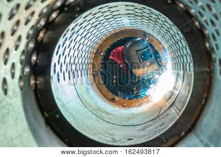 Welder welding metal pipes in tunnel made of rounded steel pipe.