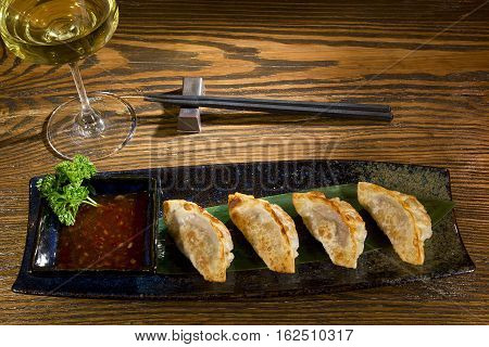 Yaki gedza with sauce in a ceramic pot on a wooden table