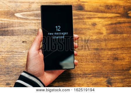 Twelve new SMS messages received notification on smartphone device held by adult female hand