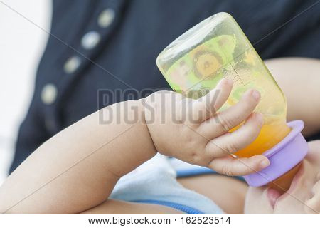 hand of baby holding orange juice bottle suck in embrace mother