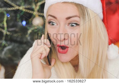 Beautiful blond girl talking on the phone in christmas settin expressing emotions